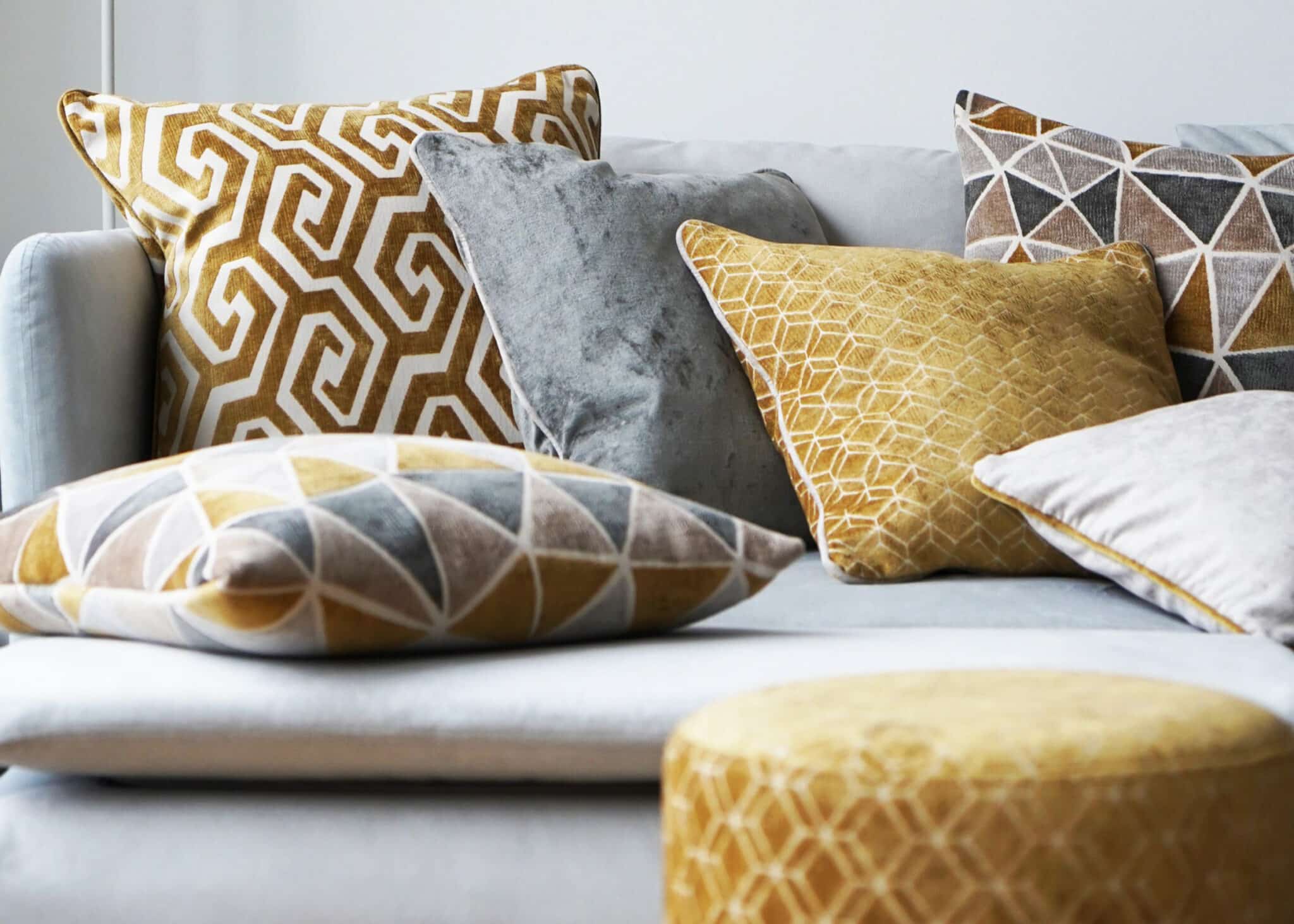 Kissen in Silber und Gold mit geometrischen Mustern auf heller Couch, daneben Vasen in verschiedenen Metalltönen.